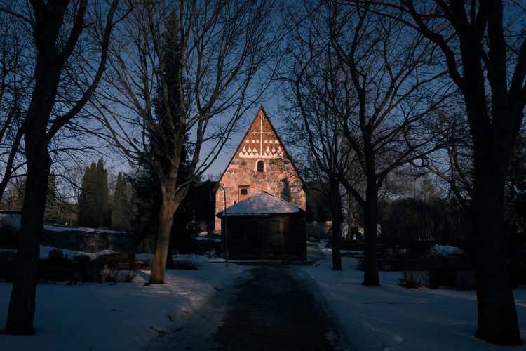 Vanajan kirkko lännestä kuvattuna, länsipääty näkyy valaistuna lumettoman ja mustan ympäristön keskeltä.