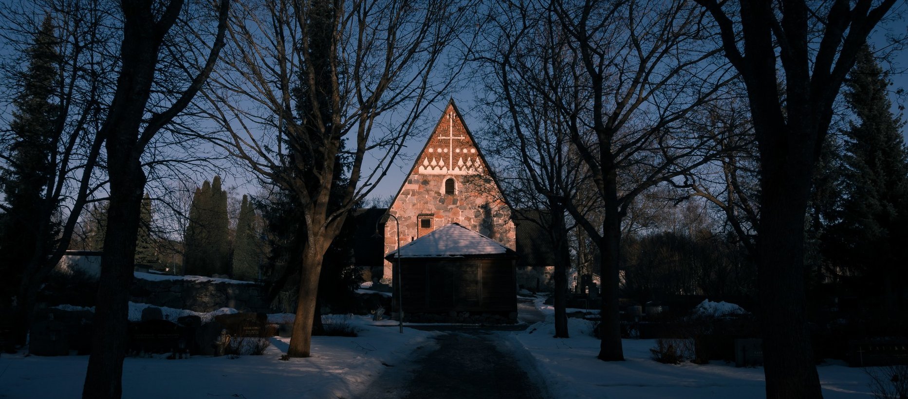 Vanajan kirkko lännestä kuvattuna, länsipääty näkyy valaistuna lumettoman ja mustan ympäristön keskeltä.