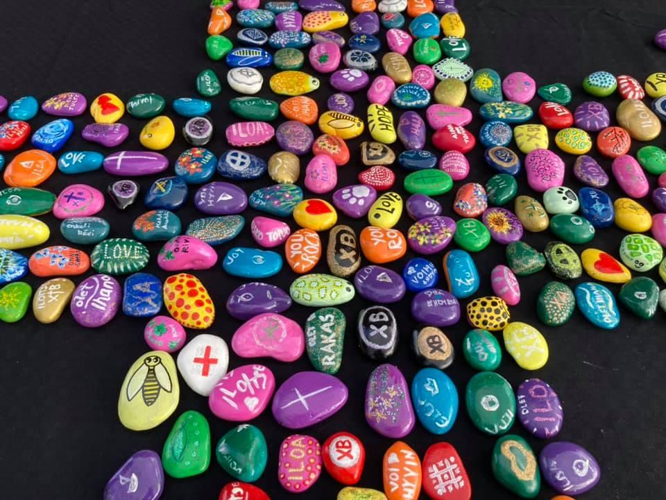 Eri värisiksi maalattuja kiviä, jotka on aseteltu ristin muotoon. Kivissä muun muassa rohkaisevia lauseita.